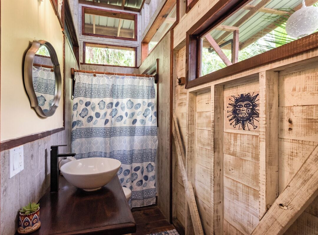 A rustic bathroom with a wooden interior, a white basin, patterned curtains, and a sun mural on the wall.