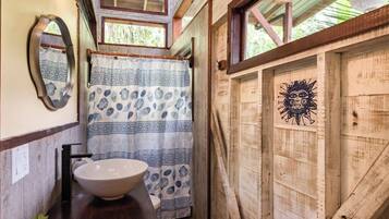 Une salle de bain rustique avec un intérieur en bois, un lavabo blanc, des rideaux à motifs et une fresque représentant un soleil sur le mur.