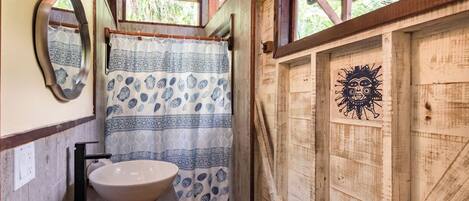 A rustic bathroom with a wooden interior, a white basin, patterned curtains, and a sun mural on the wall.