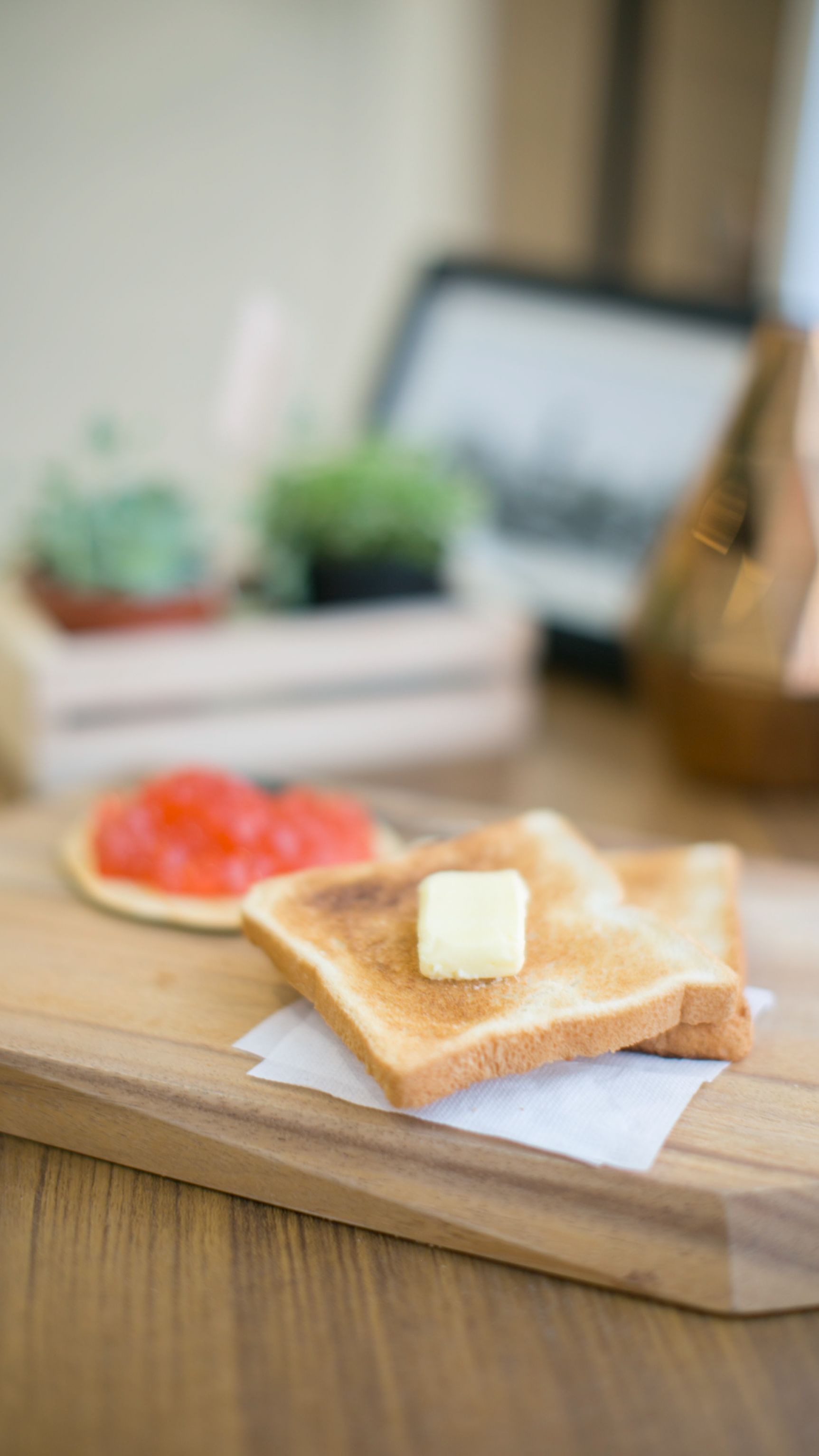 A wooden cutting board with two slices of toast, one with butter, and a slice of watermelon on a napkin.