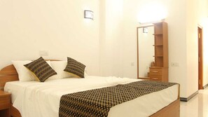 A neatly made bed with patterned pillows, a wooden nightstand, a bedside table, and a large mirror on the wall. - Ranga Holiday Resort (Aluthgama)
