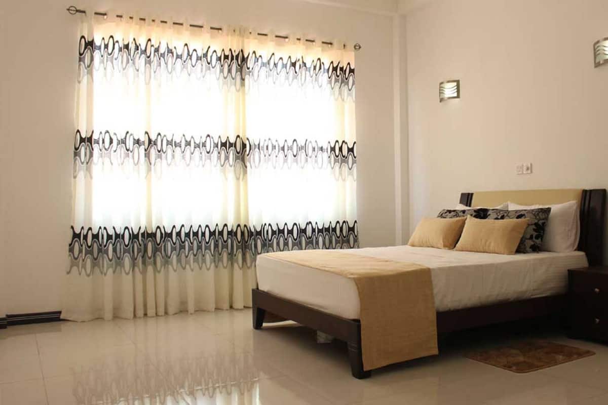 A bedroom with a bed, a nightstand, and a window with patterned curtains.