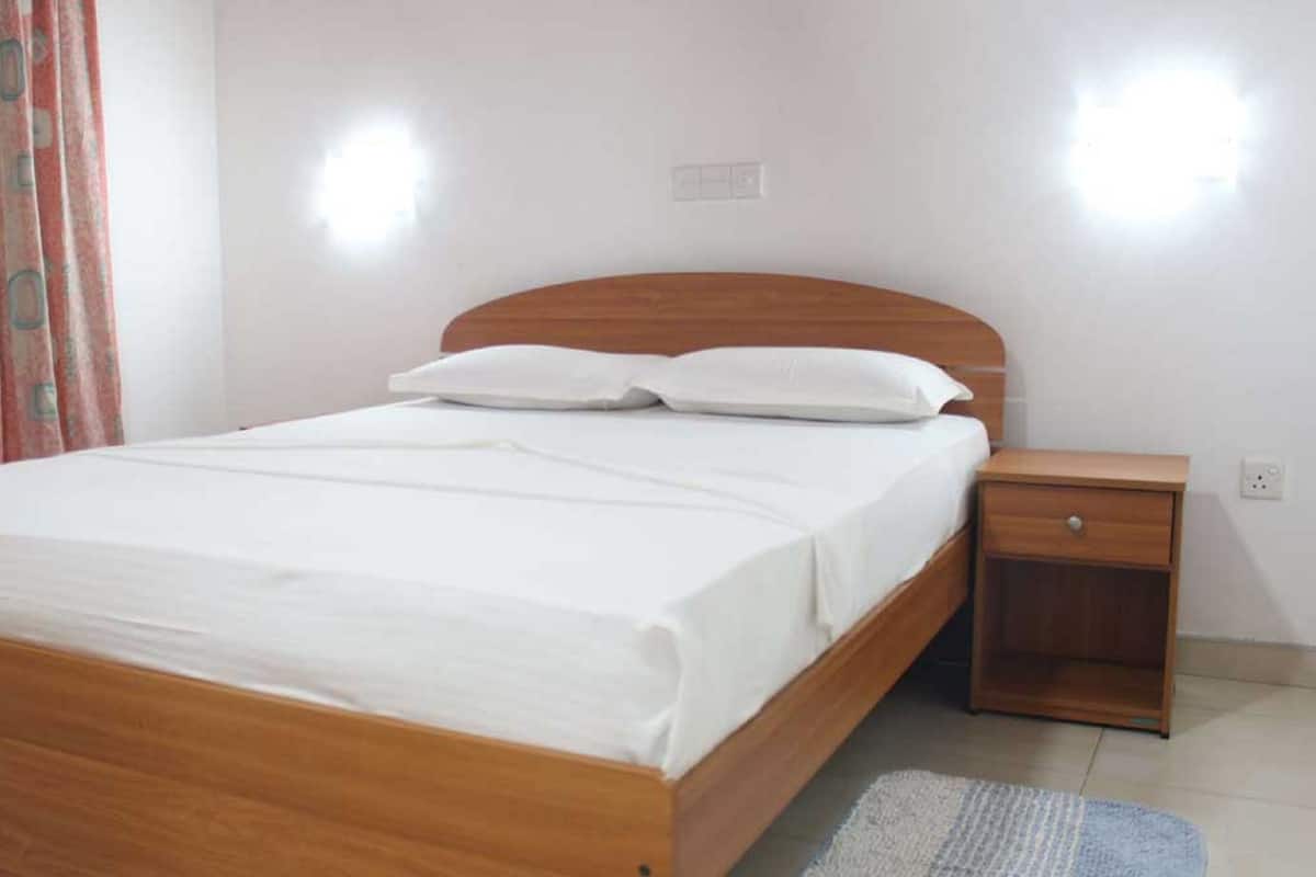 A neatly made bed with white linens, a wooden headboard, and a small bedside table with a drawer.