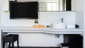 A modern bathroom with a large mirror, a flat-screen TV, a white sink, and a black trash bin. - Modena B&B (Taitung)