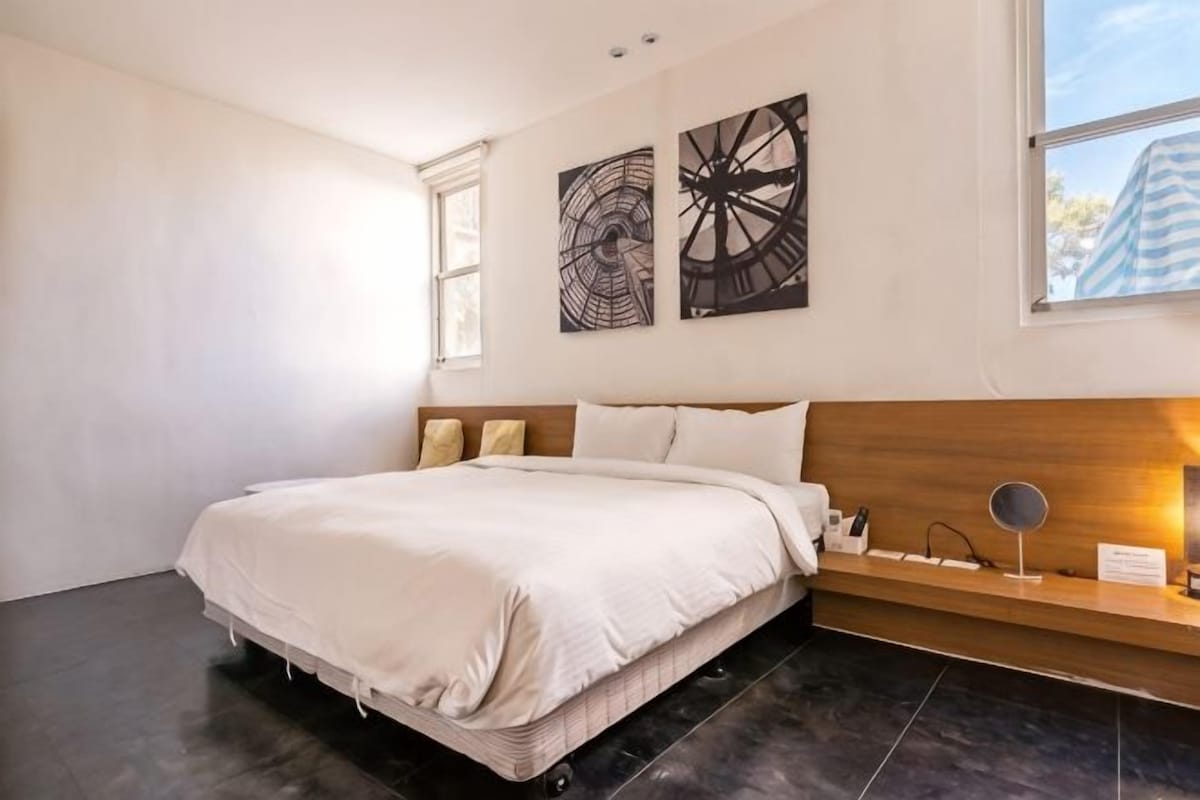 A modern bedroom with a large bed, a wooden headboard, a bedside table, and two abstract wall art pieces.