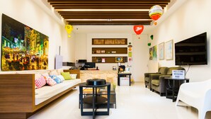 A modern hotel room with a sofa, a small table, a TV, and a desk. There are balloons and a painting on the wall. - Modena B&B (Taitung)