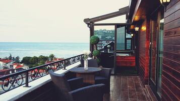 Enjoy the ocean view from this balcony with wicker furniture, a small table, and a potted plant.