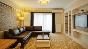 A hotel room with a sofa, a coffee table, a television, and a patterned carpet. - My Suit Residence (Atakum)