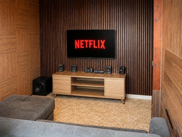 A modern living room with a wooden wall paneling, a flat-screen TV displaying 'NETFLIX', a wooden entertainment unit with speakers, and a patterned carpet. - My Suit Residence (Atakum)