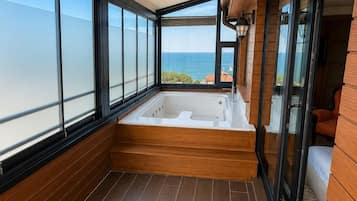 A balcony with a wooden floor, a large window, and a view of the sea.
