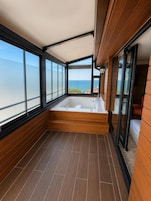 Un balcón con piso de madera, un ventanal grande y vista al mar.