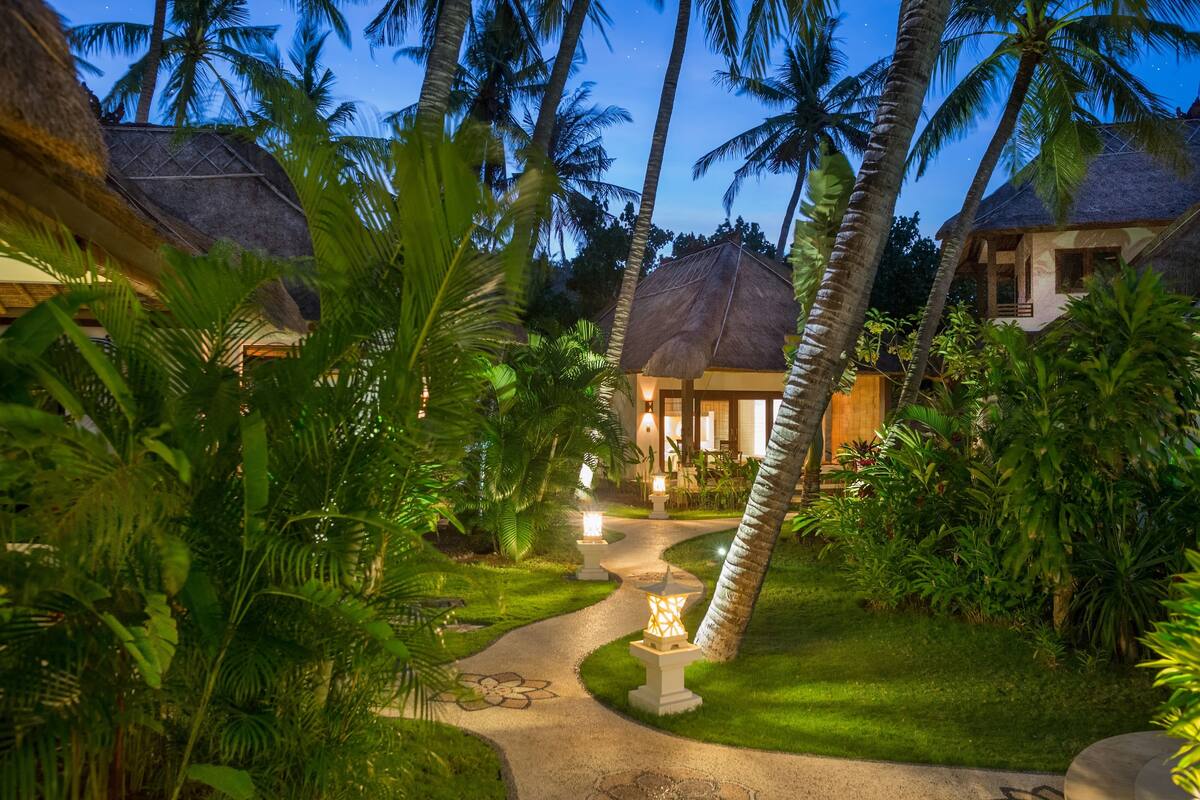 Un complexe hôtelier tropical doté de villas aux toits de chaume, d’un sentier dallé et d’une végétation luxuriante.