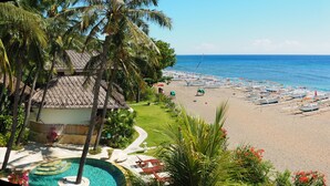 A beach with a pool, lounge chairs, and boats. - Palm Garden Amed Beach & Spa Resort Bali (Karangasem)