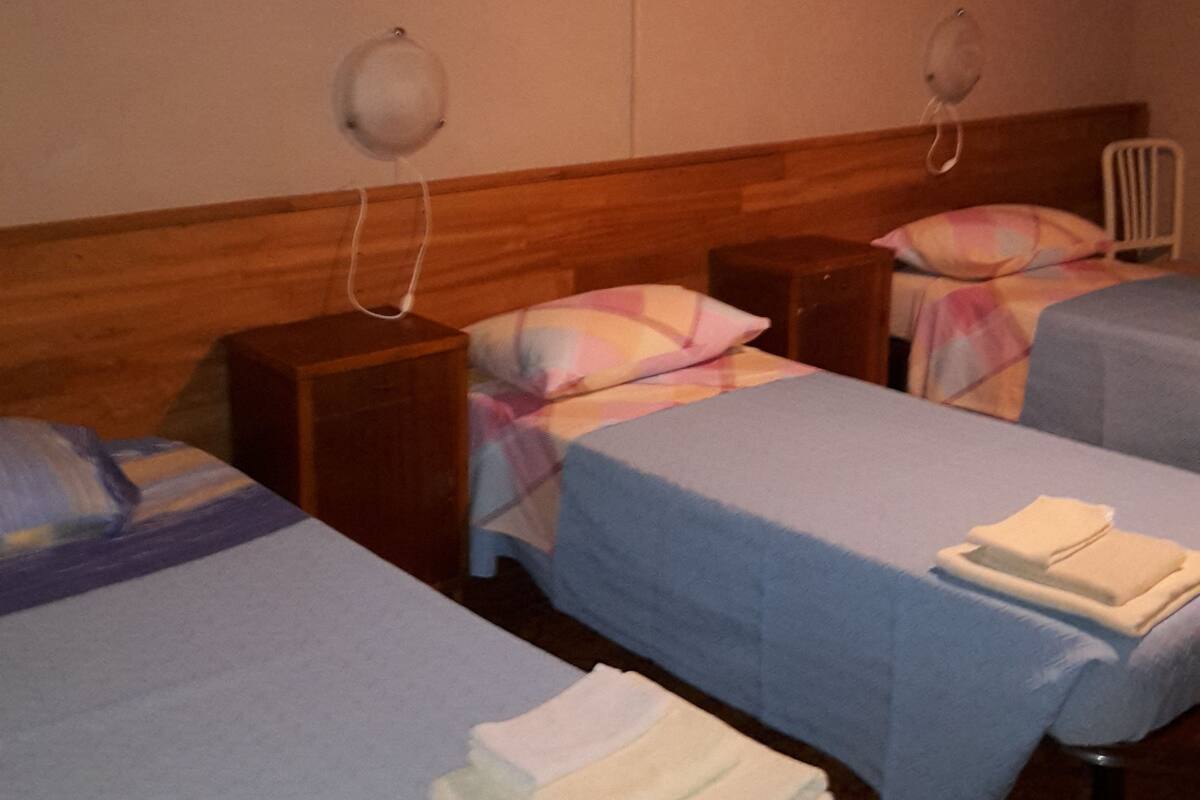 Een hotelkamer met twee eenpersoonsbedden, elk met een kussen en een nachtkastje. Boven elk bed is een wandlamp bevestigd en aan de muur staat een radiator.