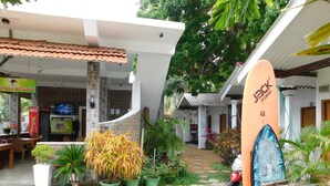 A courtyard with a reception area, a surfboard, and potted plants. - The Bavarian Resort (Arugam Bay)