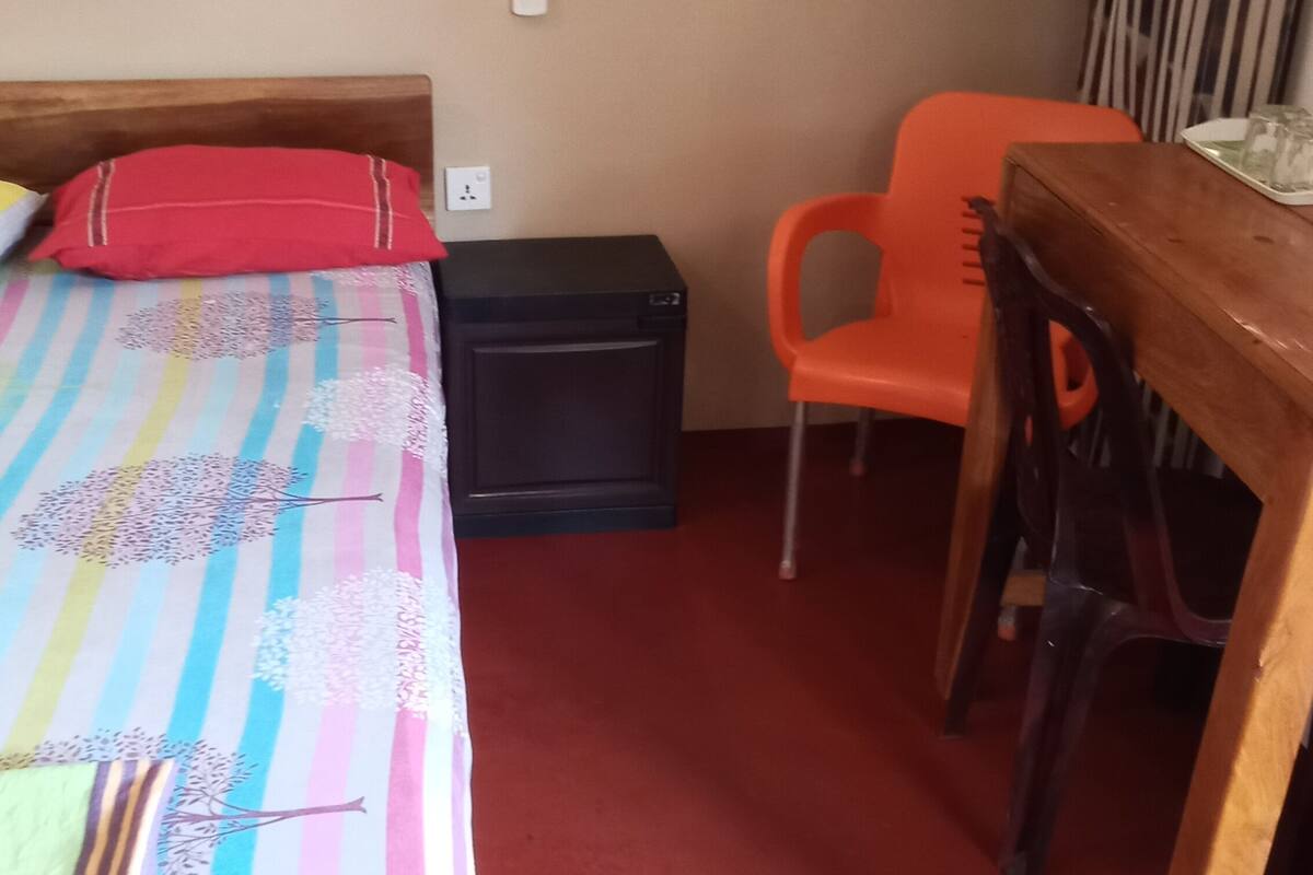 Quarto com cama, escrivaninha, cadeira e um pequeno armário preto.