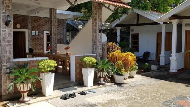 A covered outdoor area with a brick wall, a wooden table, and several potted plants. - The Bavarian Resort (Arugam Bay)
