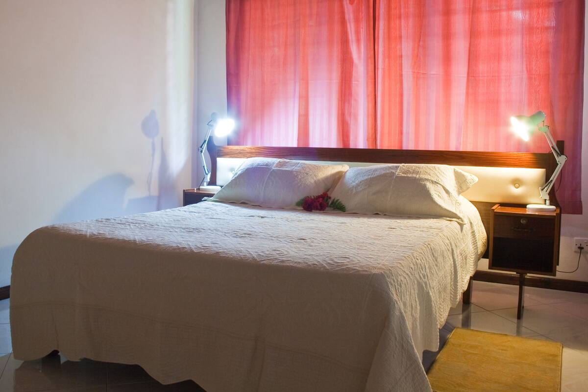 Una cama bien tendida con una colcha blanca, dos lámparas de noche y una mesita de noche de madera.