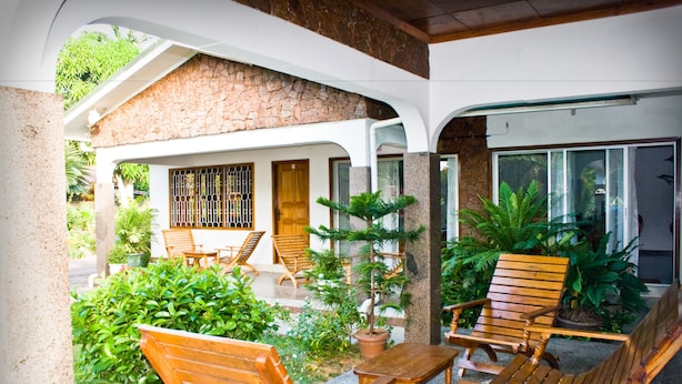 A covered outdoor seating area with wooden furniture and potted plants. - Villa de Roses (Mahé Island)