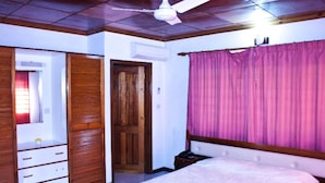 A bedroom with a bed, a wardrobe, a ceiling fan, and a window with curtains. - Villa de Roses (Mahé Island)