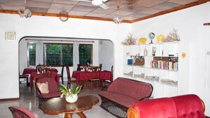 A spacious living area with a dining table, red upholstered chairs, a red sofa, and a bookshelf. - Villa de Roses (Mahé Island)