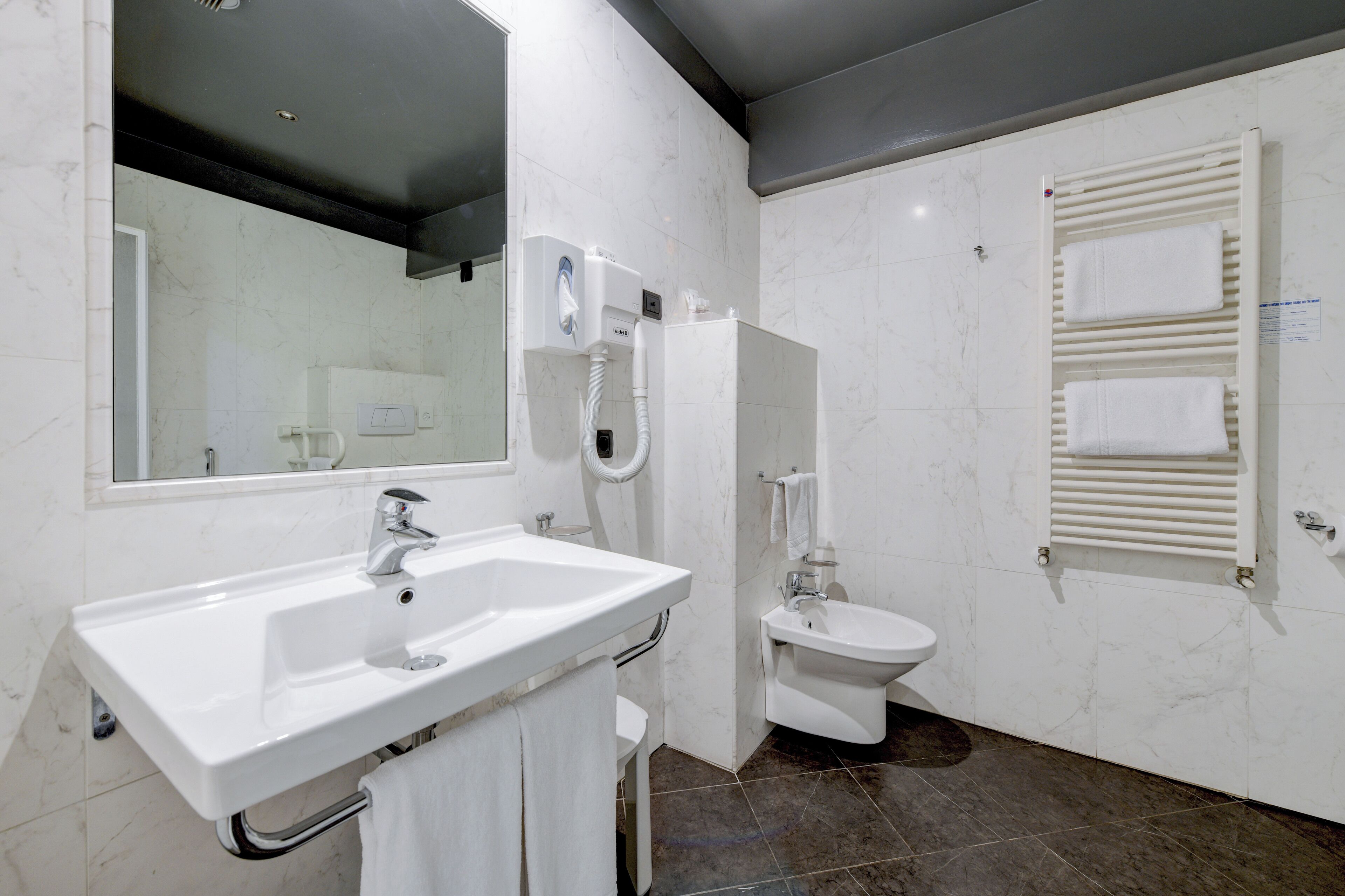 A modern bathroom with a white sink, a mirror, a toilet, and a towel warmer.