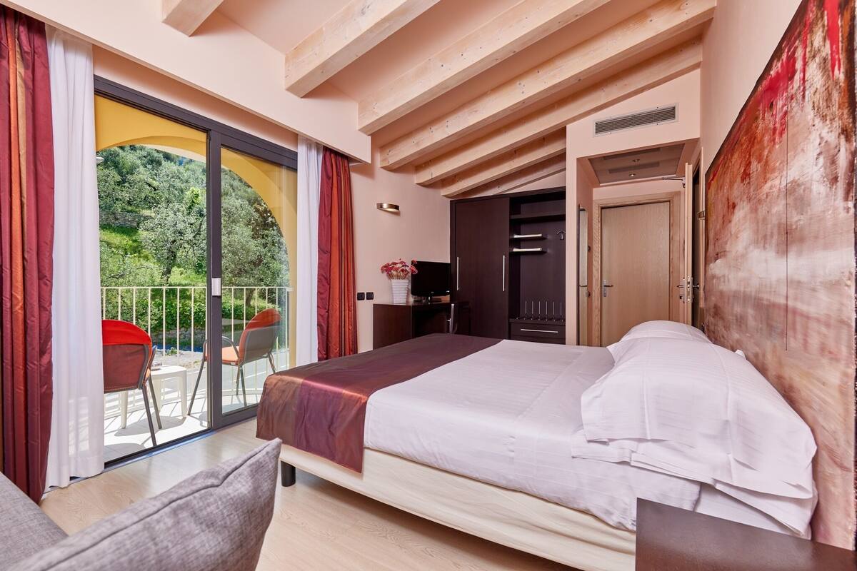Une chambre d’hôtel moderne avec un grand lit, un balcon orné de rideaux rouges et une vue sur la verdure.