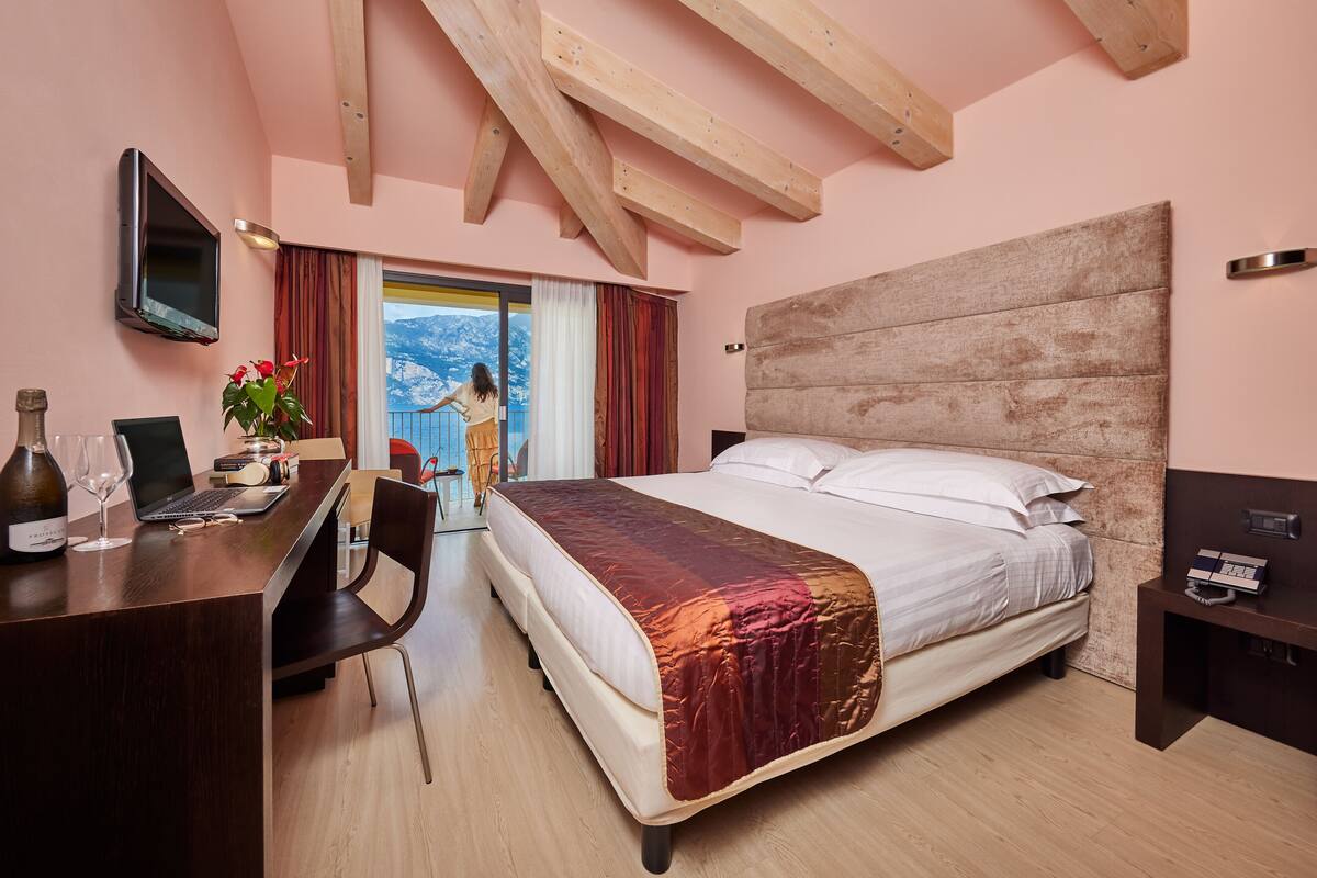 Une chambre à coucher avec un lit, un bureau avec un ordinateur portable, une bouteille de vin et une plante.