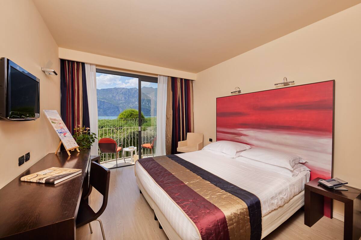 Une chambre d’hôtel avec un grand lit, un bureau avec une chaise, une télévision et une vue sur les montagnes par la fenêtre.