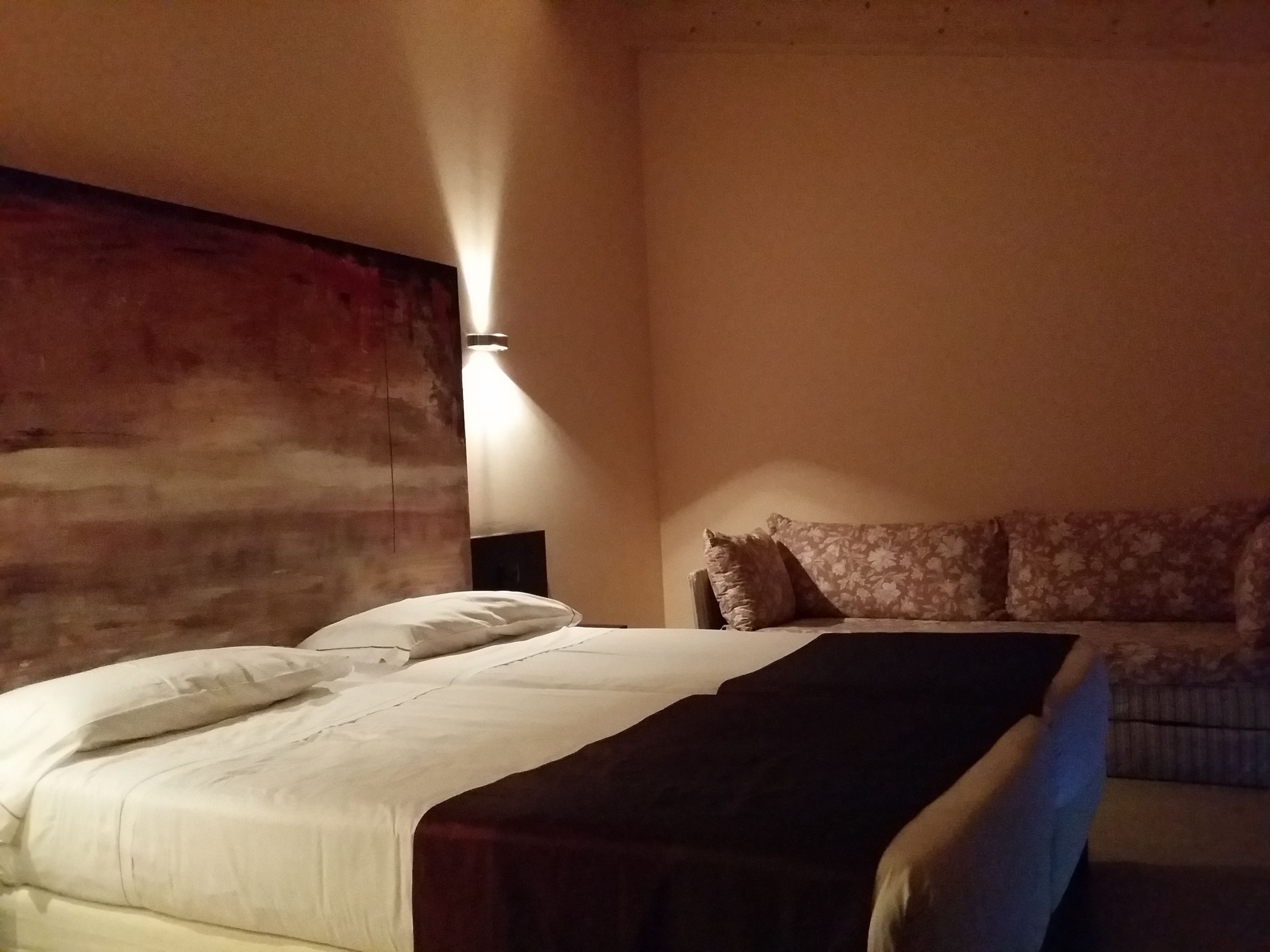 A hotel room with a large bed, a nightstand, and a sofa.