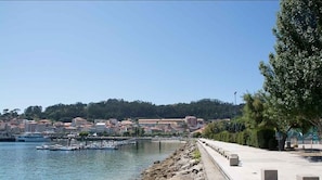 A coastal town with a marina, stone pathway, and buildings with red-tiled roofs.