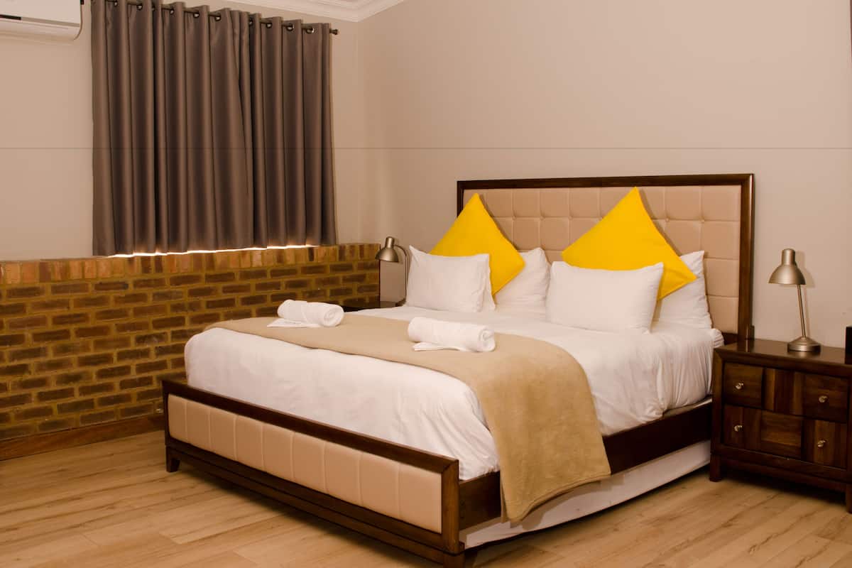 A neatly made bed with a headboard, a wooden nightstand, and a brick wall.