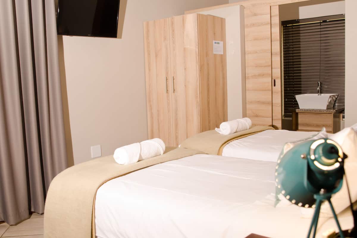 A hotel room with two beds, a wooden wardrobe, a bathroom with a sink, and a flat-screen TV mounted on the wall.