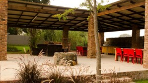 Un espace extérieur aménagé en terrasse, avec un barbecue en briques, des chaises rouges et une table en pierre.