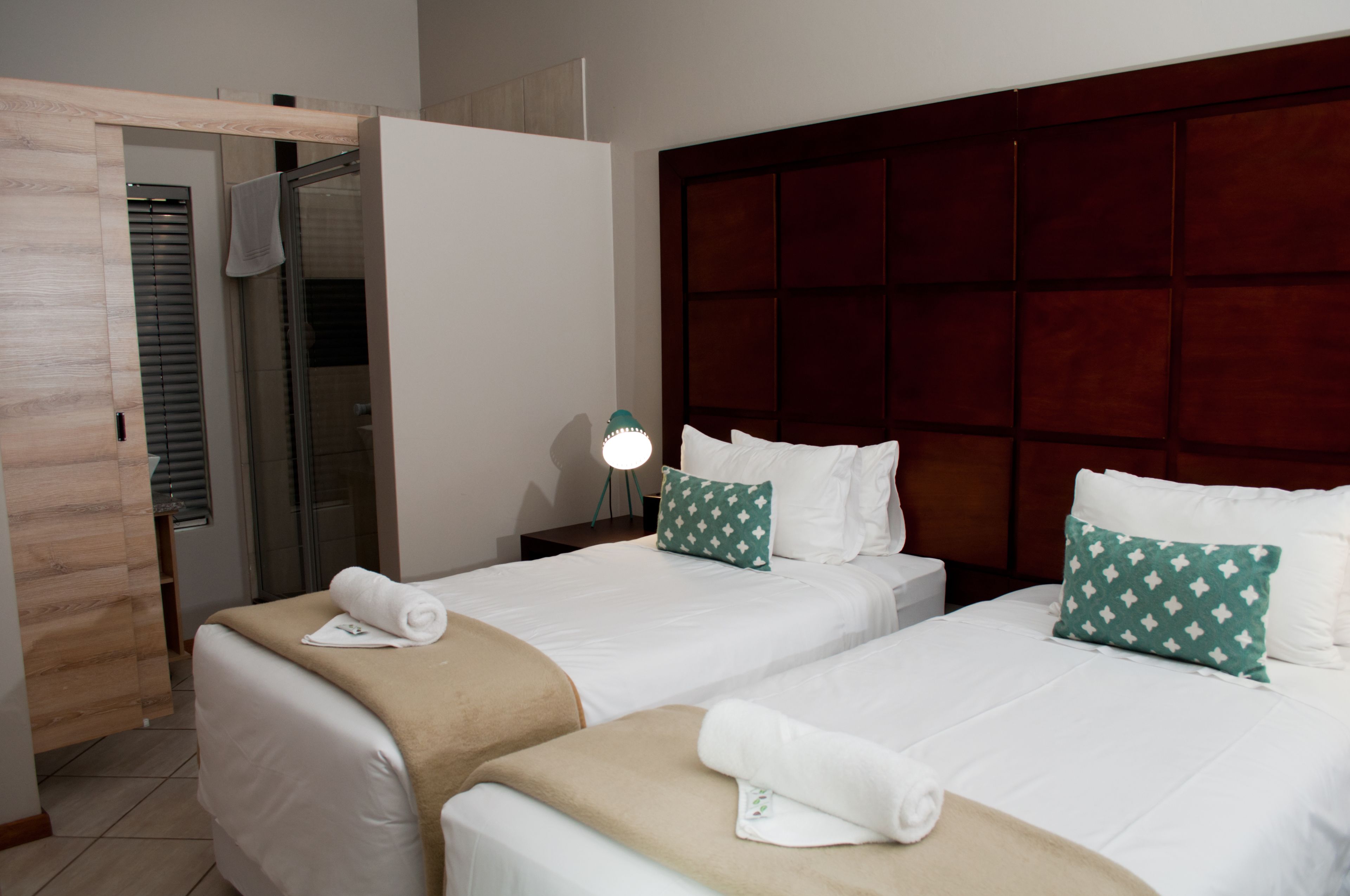 A hotel room with two beds, a wooden door, a glass shower, and a bedside lamp.