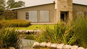 Un bâtiment moderne avec une façade en pierre, un toit plat et un petit étang au premier plan.