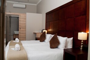 Una habitación de hotel con una cama grande, un cabecero de madera, un escritorio con una lámpara y un ordenador portátil sobre el escritorio.