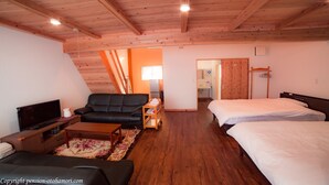 Ein gemütliches Zimmer mit Sofa, Fernseher, kleinem Tisch, Bett und Holzboden.