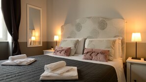 A hotel room with a bed, two bedside lamps, a mirror, and a window with curtains. - B&B Le Cupole di Trieste (Trieste)