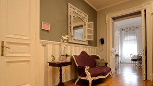 A hallway with a wooden floor, a purple armchair, a small table with a vase and a plant, and a mirror on the wall. - B&B Le Cupole di Trieste (Trieste)