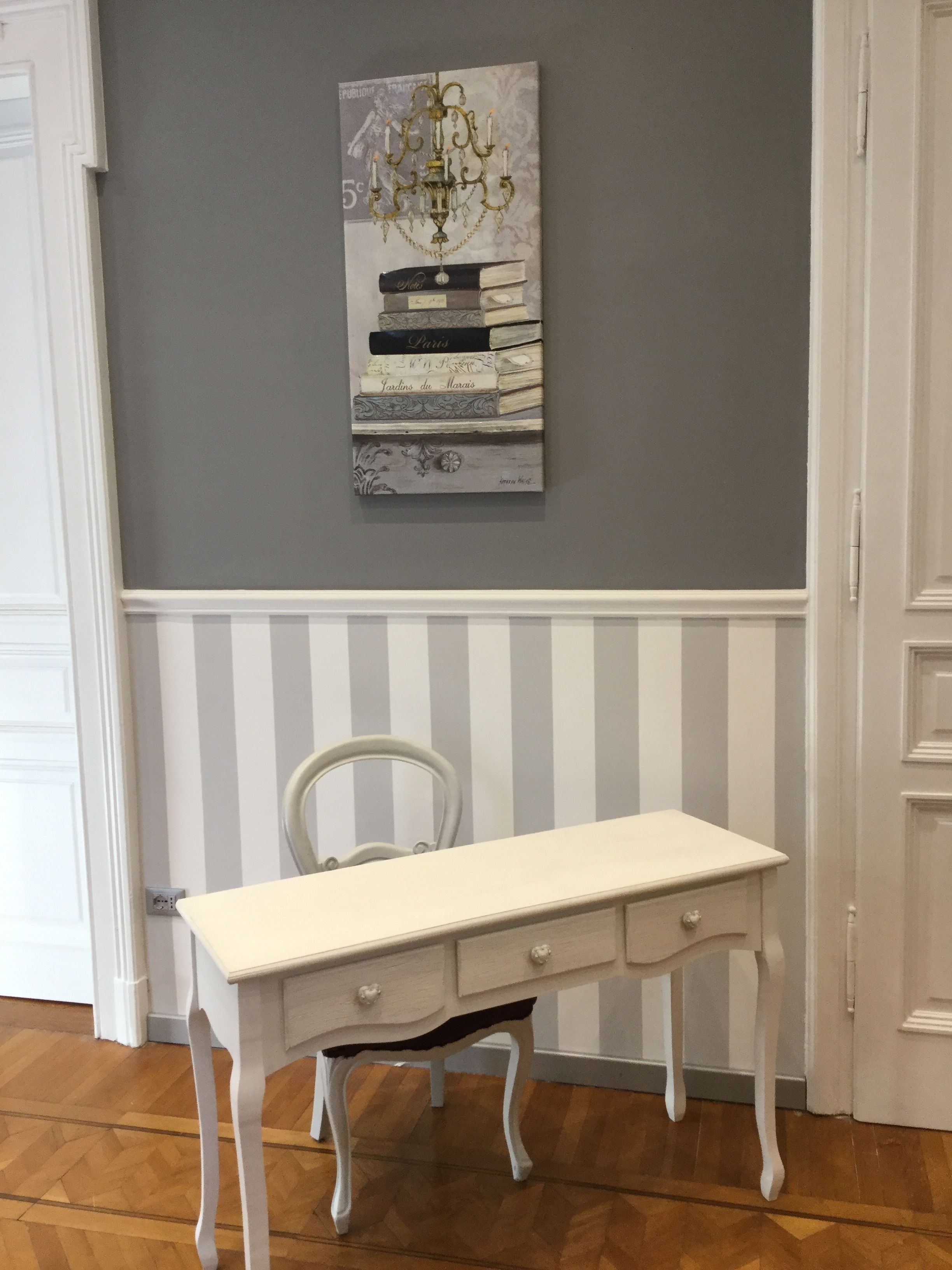 A white desk with drawers, a white chair, and a wall-mounted decorative piece above it.