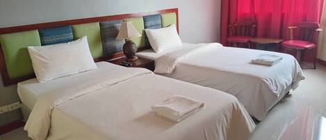 A hotel room with two beds, a nightstand with a lamp, a red curtain, and a small table with chairs.