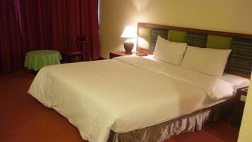 A hotel room with a large bed, a small table, a chair, and a nightstand with a lamp.