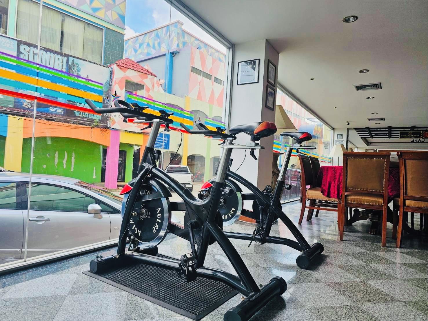 An indoor cycling area with stationary bikes, a car parked outside, and a view of colorful buildings.