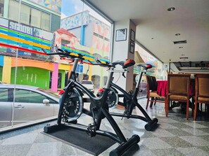An indoor cycling area with stationary bikes, a car parked outside, and a view of colorful buildings.