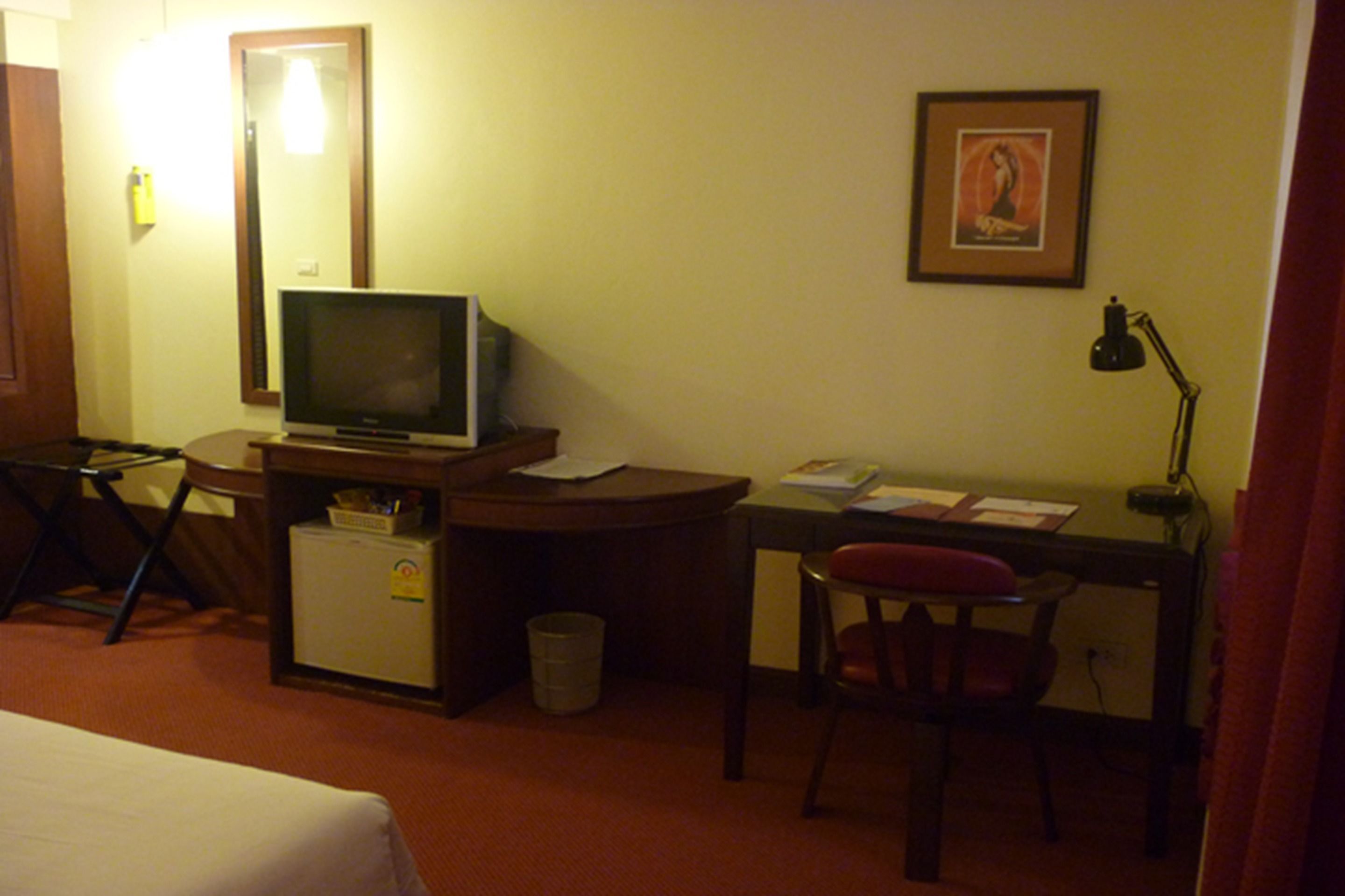 Une chambre d’hôtel équipée d’un lit, d’un bureau avec un ordinateur, d’une chaise, d’un petit réfrigérateur et d’une télévision.
