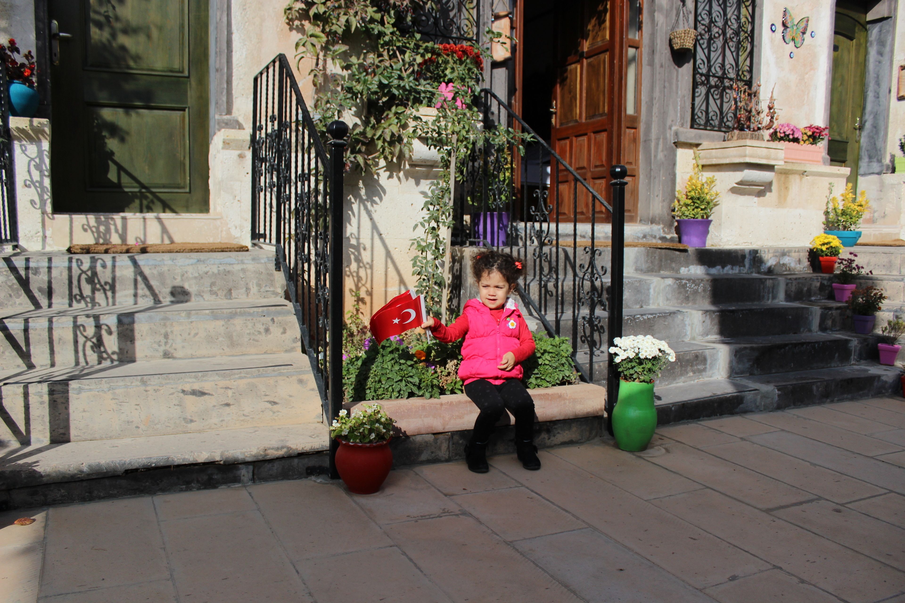 A child sitting on a bench outside a building with steps and potted plants.