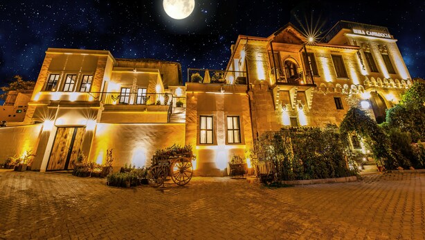Un bâtiment historique doté d’une entrée imposante, illuminée d’une lumière chaleureuse, et une pleine lune dans le ciel nocturne.