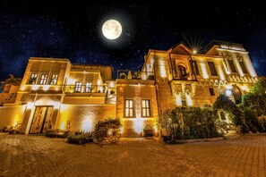 Ein historisches Gebäude mit einem markanten Eingang, beleuchtet durch warmes Licht, und einem Vollmond am Nachthimmel.
