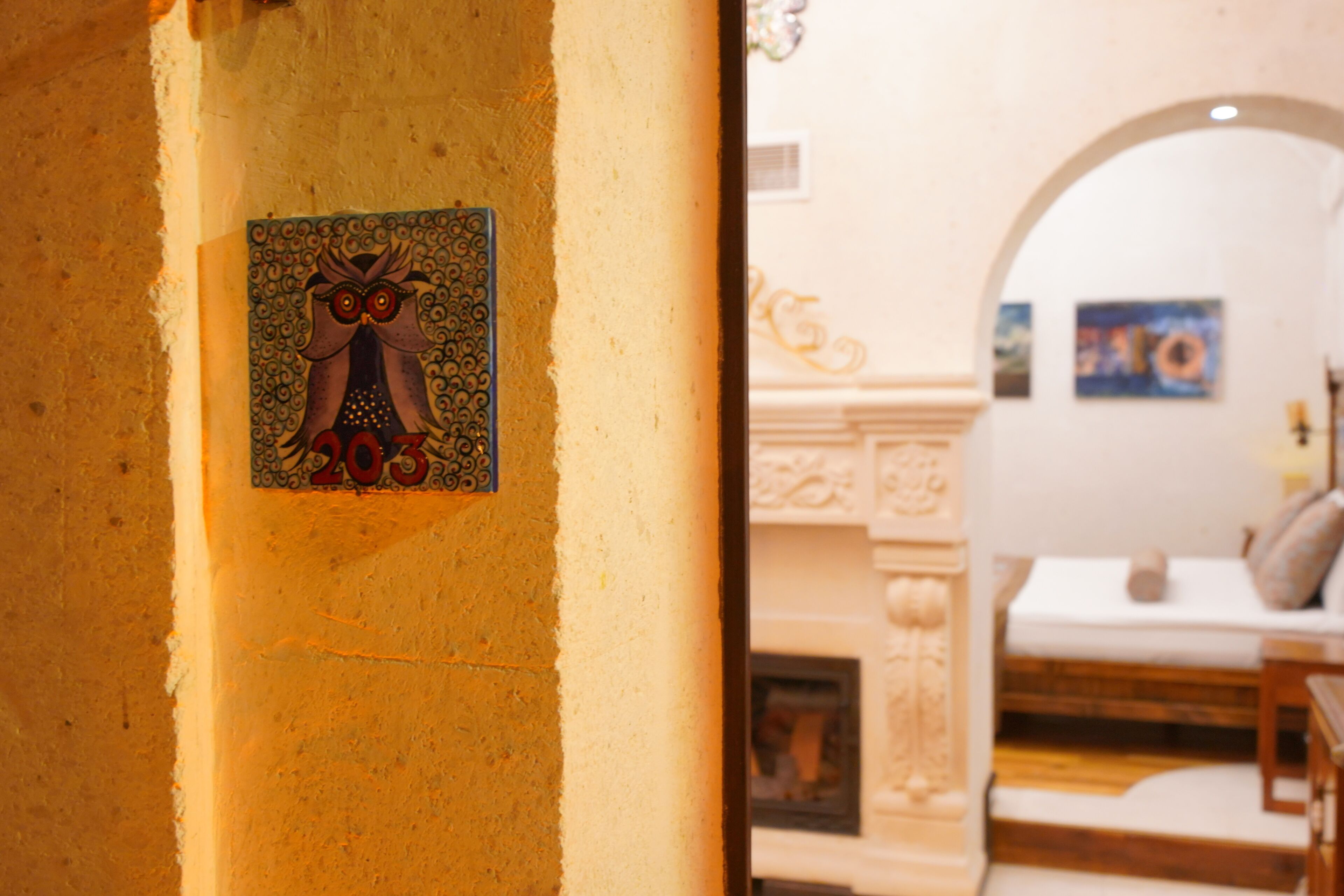 A wall-mounted decorative plate with a bird design, a fireplace with intricate carvings, and a white sofa in a warmly lit room.